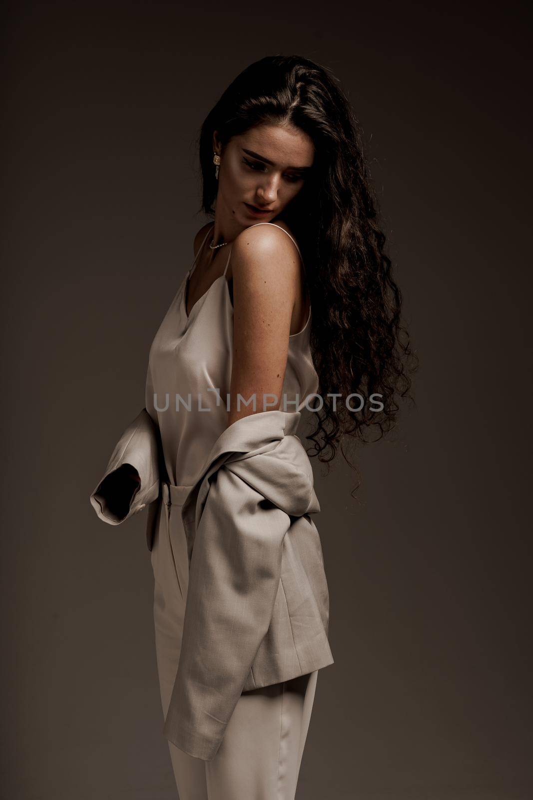 Fashion, elegant and sexy professional model in studio. Gorgeous young female in classic suit in photostudio. Attractive girl with curly hair posing.