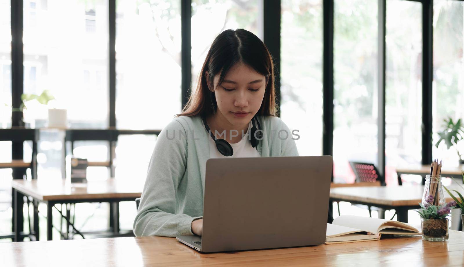 Serious focused Asian student using laptop in kitchen, looking at screen with attention and concentration, watching learning webinar, virtual training, video course, studying from home by wichayada