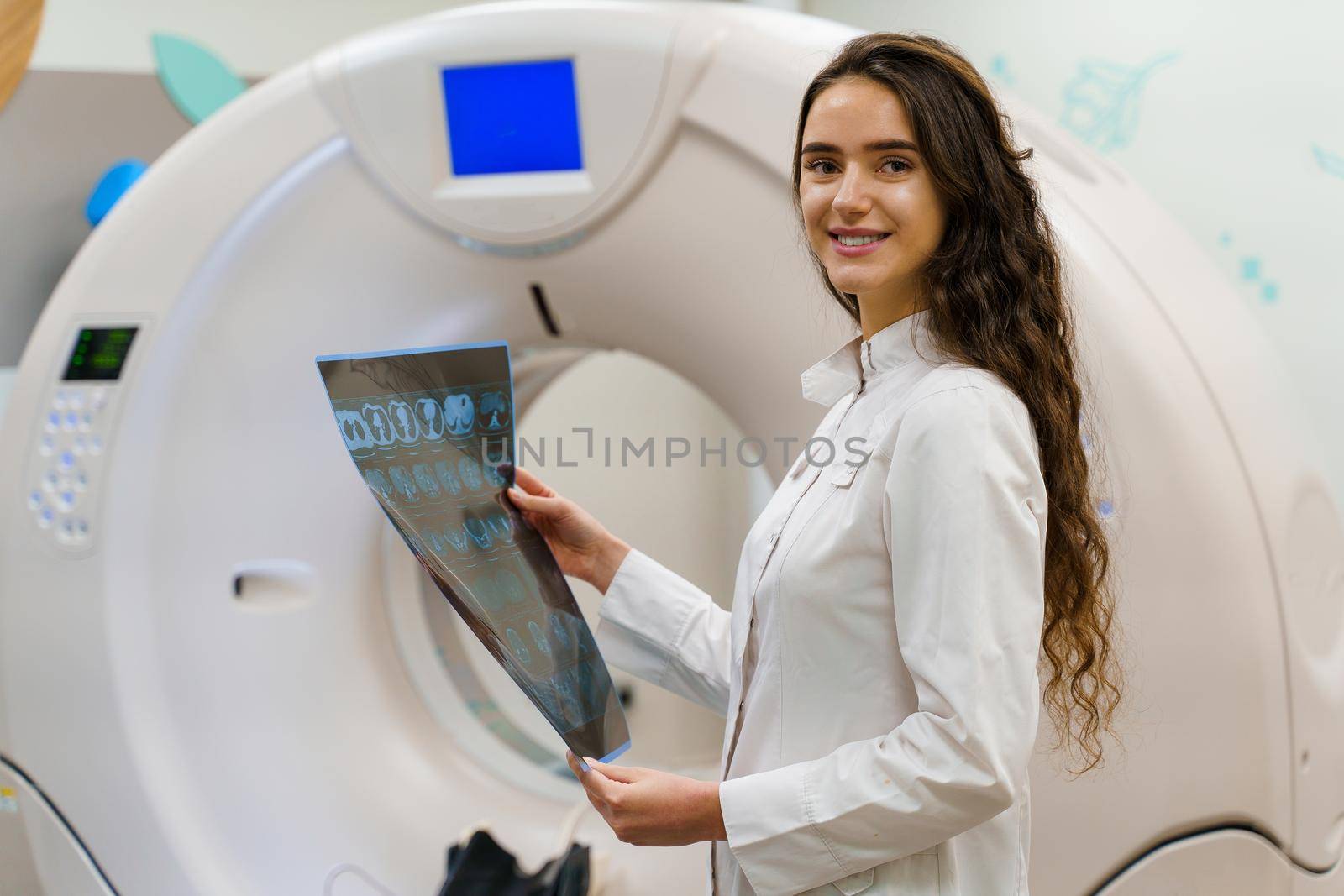 Medical student looks in camera and smile. Medical stands with x-ray picture of patient brain in her hands. woman stays in front of kt komputer tomograhphy