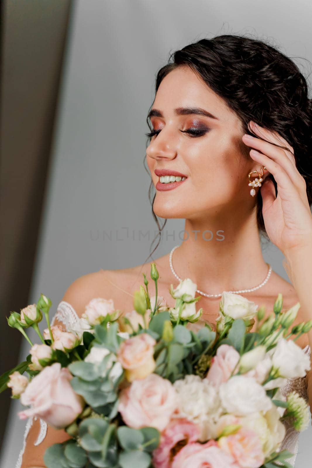 Bride with wedding bouquet smiles and touches her face and hair. Attractive girl portrait for social networks. Girl in wedding gown on blank background. by Rabizo