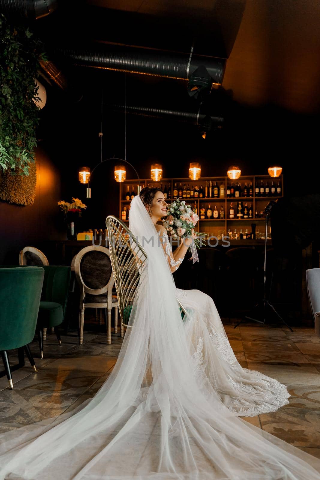 Bride in wedding dress and bridal veil seats on fashion chair in cafe. Advert for social networks for wedding agency and bridal salon by Rabizo