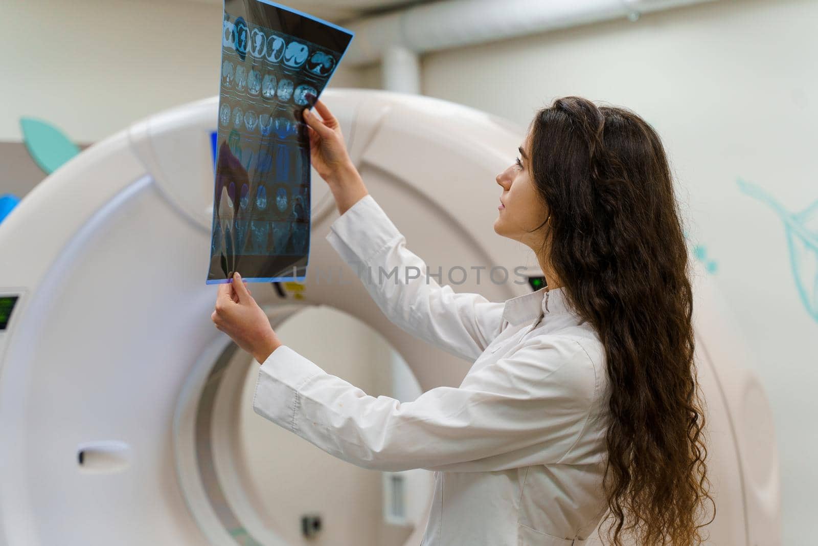 Medical doctor looks at x-ray picture of patient brain near kt komputer tomograhphy. Young girl in medical clinic gotes new expirience