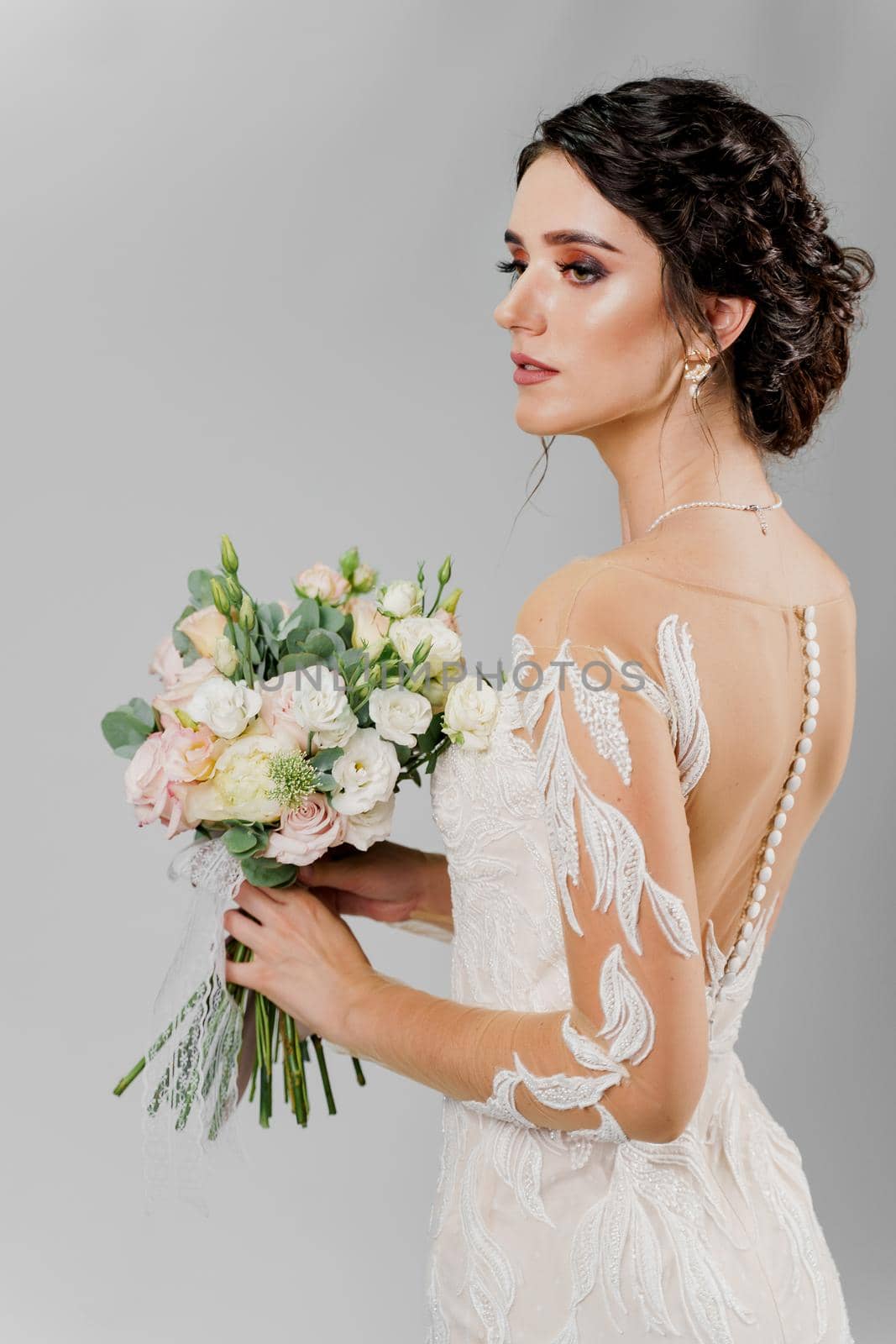 Bride in wedding dress holds bouquet and looks left side in studio on blank background. Attractive girl portrait
