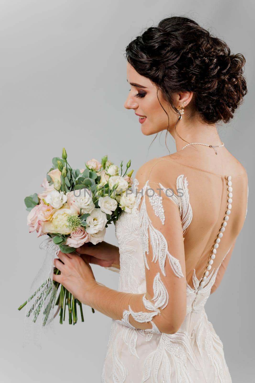 Bride in wedding dress holds and looks at bouquet io on blank background. Attractive girl portrait. Vertical photo for advert in social networks and wedding salon