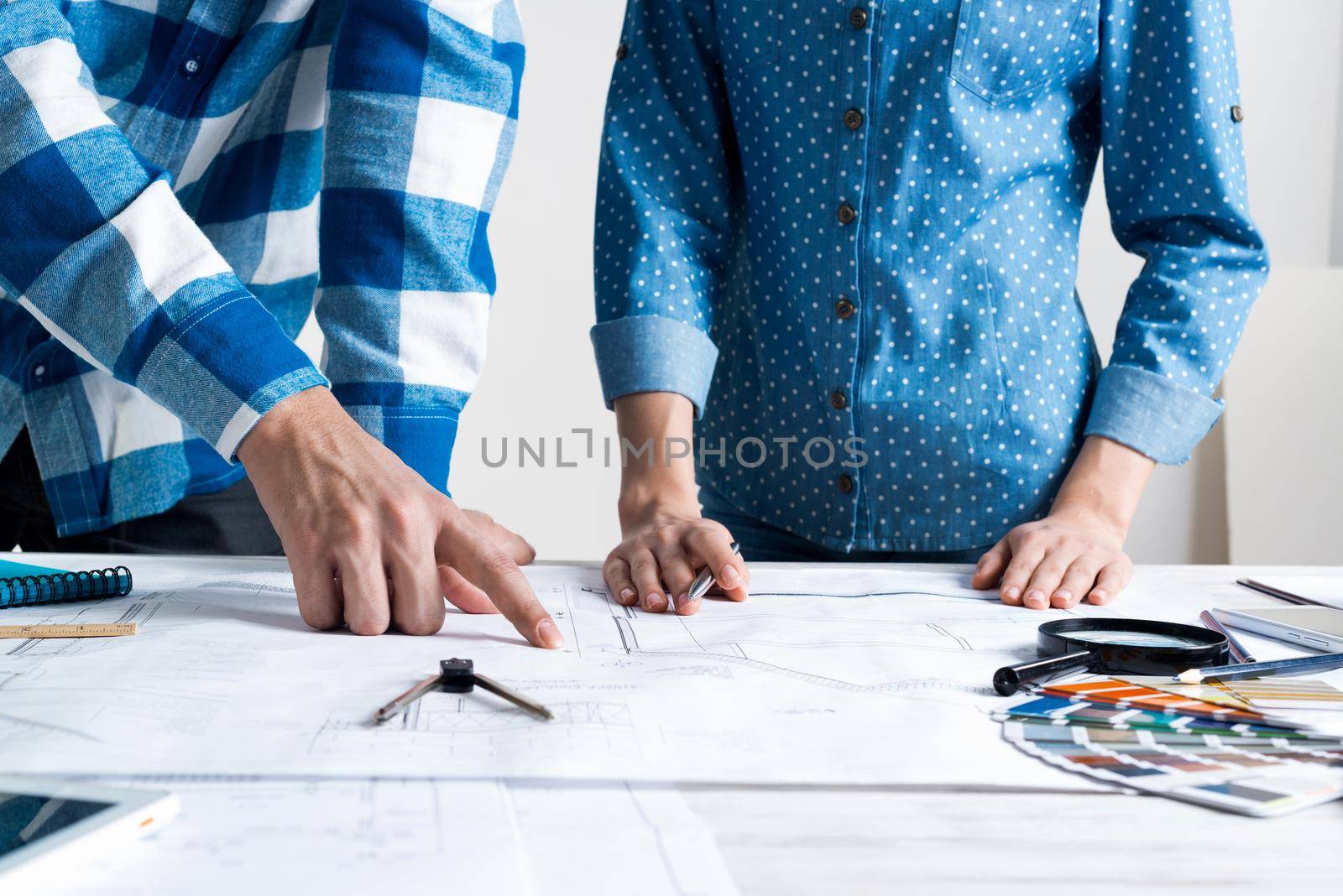 Man and woman together working at design project. Creative teamwork at workspace with construction blueprint and color swatches. People standing near desk and discussing in architecture studio.