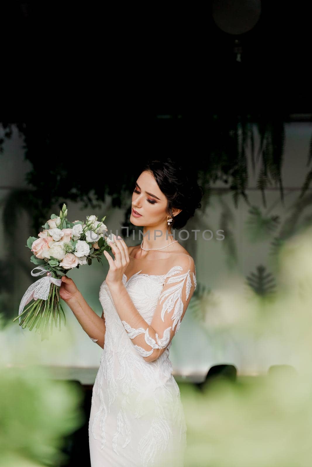 Bride with wedding bouquet smiles and touches her face. Attractive girl portrait for social networks. Girl in wedding dress in luxury restaurant by Rabizo