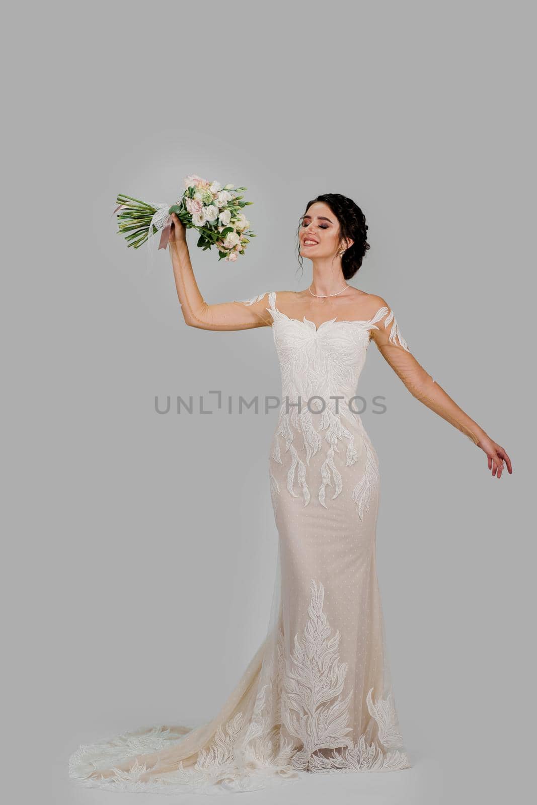 Bride with wedding bouquet smiles with closed eyes. Vertical photo for social networks. Girl in wedding gown on blank background. by Rabizo