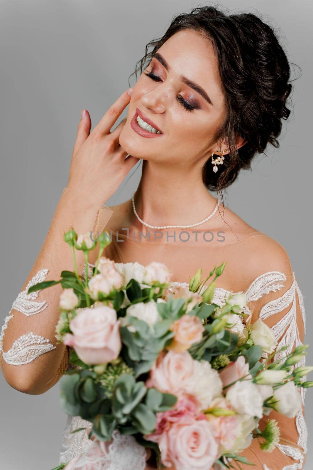 Bride with wedding bouquet smiles and touches her face and hair. Attractive girl portrait for social networks. Girl in wedding gown on blank background. by Rabizo