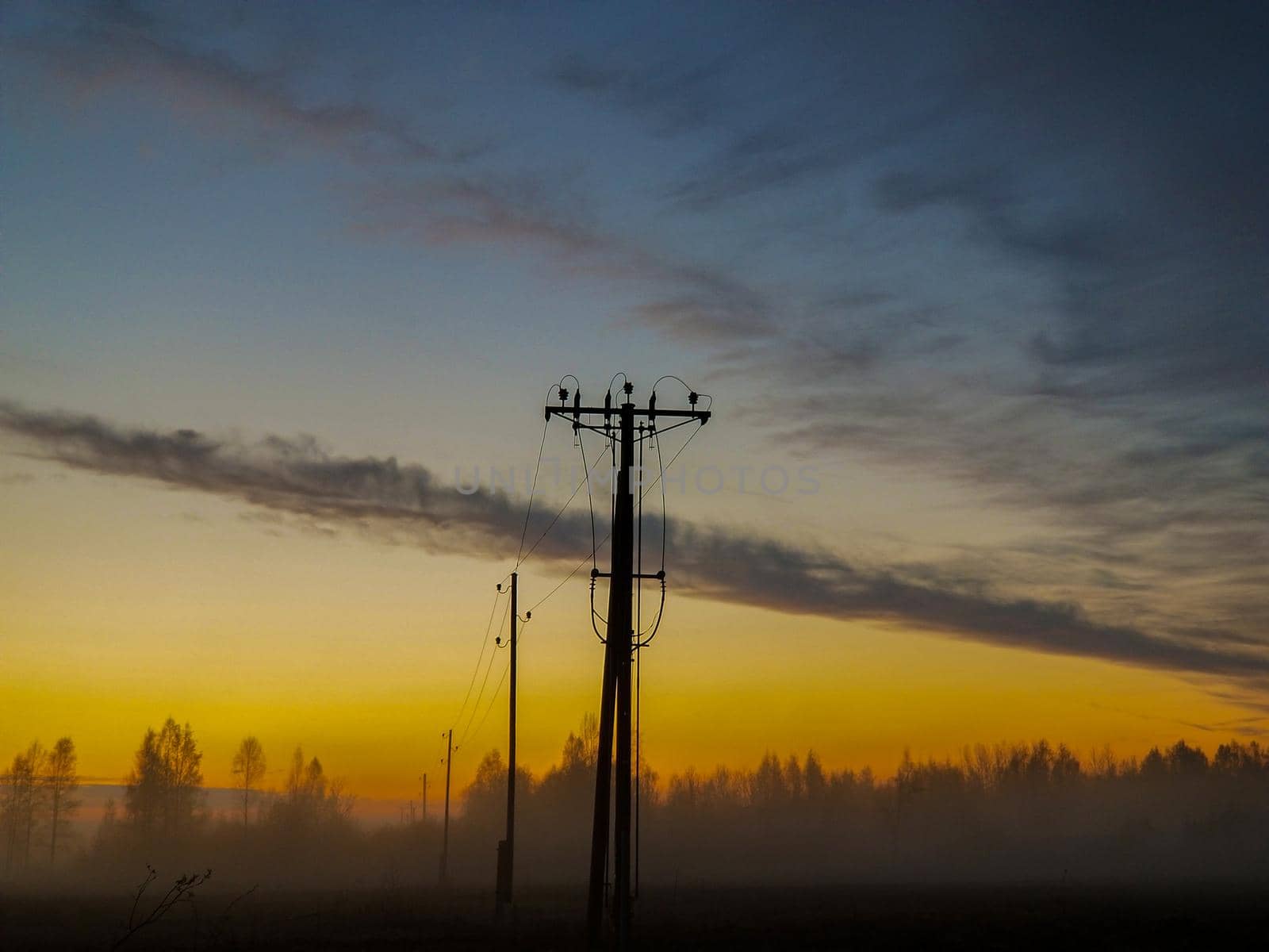 high voltage carrier power line in the fog against the background of a cloudy sky during sunrise