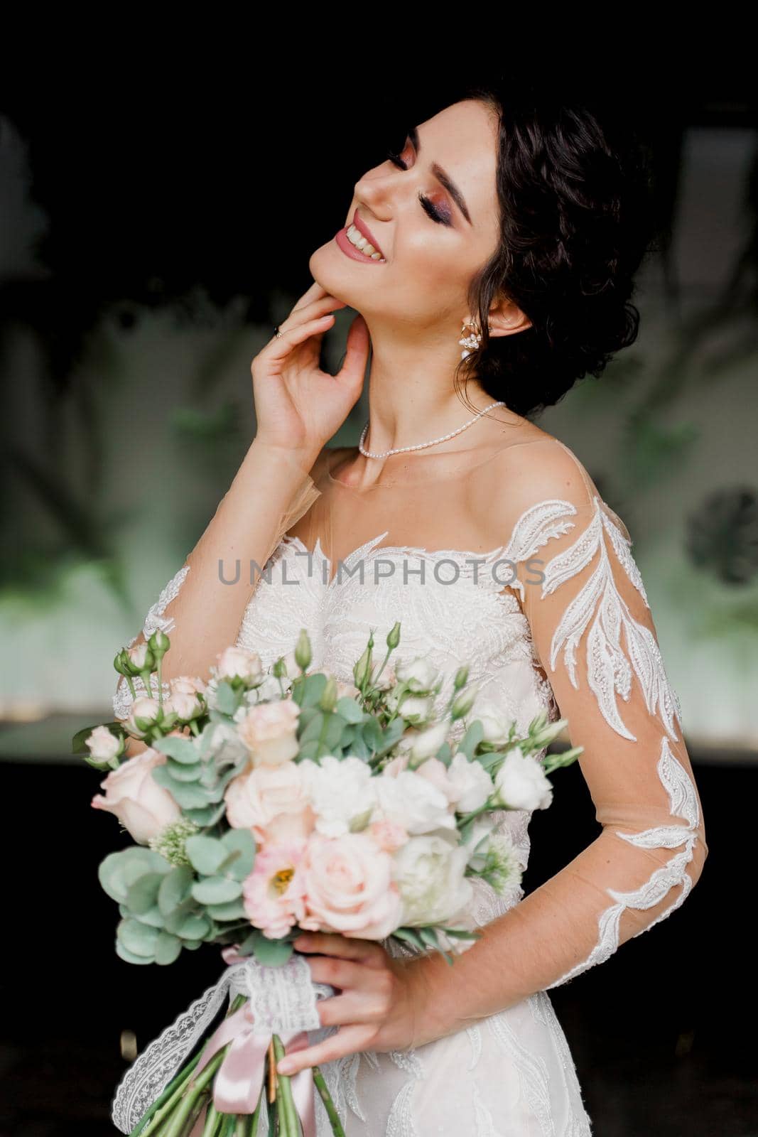 Bride with wedding bouquet smiles and touches her face and hair. Girl in wedding dress in fashion restaurant. by Rabizo