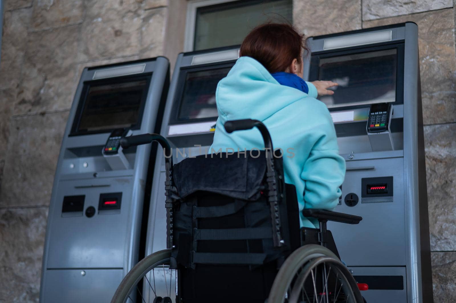 A Caucasian woman in a wheelchair does not reach the self-service checkout at the railway station. Hard-to-reach environment