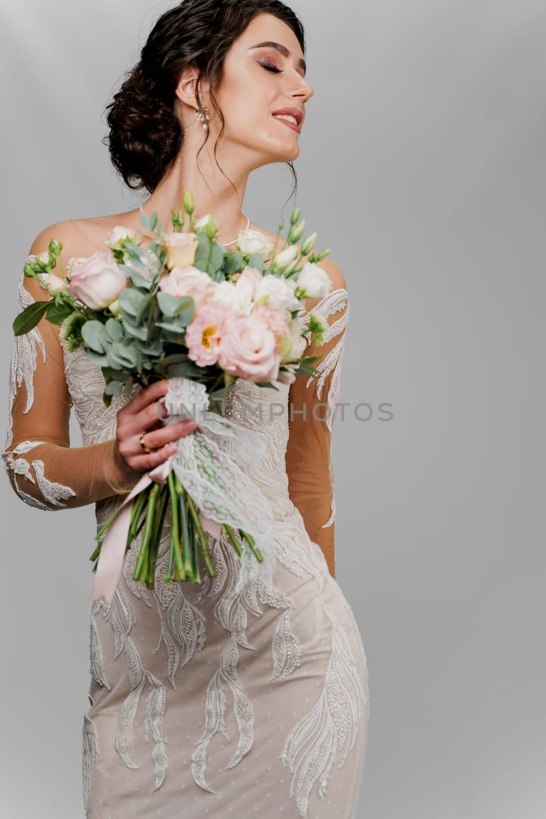 Bride with wedding bouquet looks right side. Attractive girl vertical portrait for social networks. Girl in wedding gown on blank background