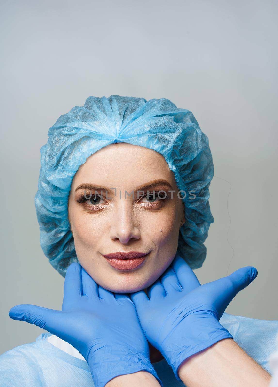 Consultation with plastic surgeon on white background. Cosmetic rejuvenating facial treatment. Doctor man with blue medical gloves touches girl face.