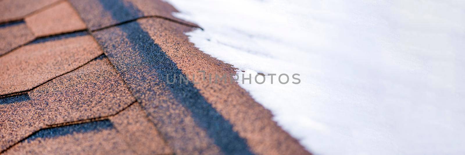 Red shingles. The roof of a house made of shingles is covered with snow in winter, close-up. Frost resistance and elasticity of bituminous tiles in severe frosts