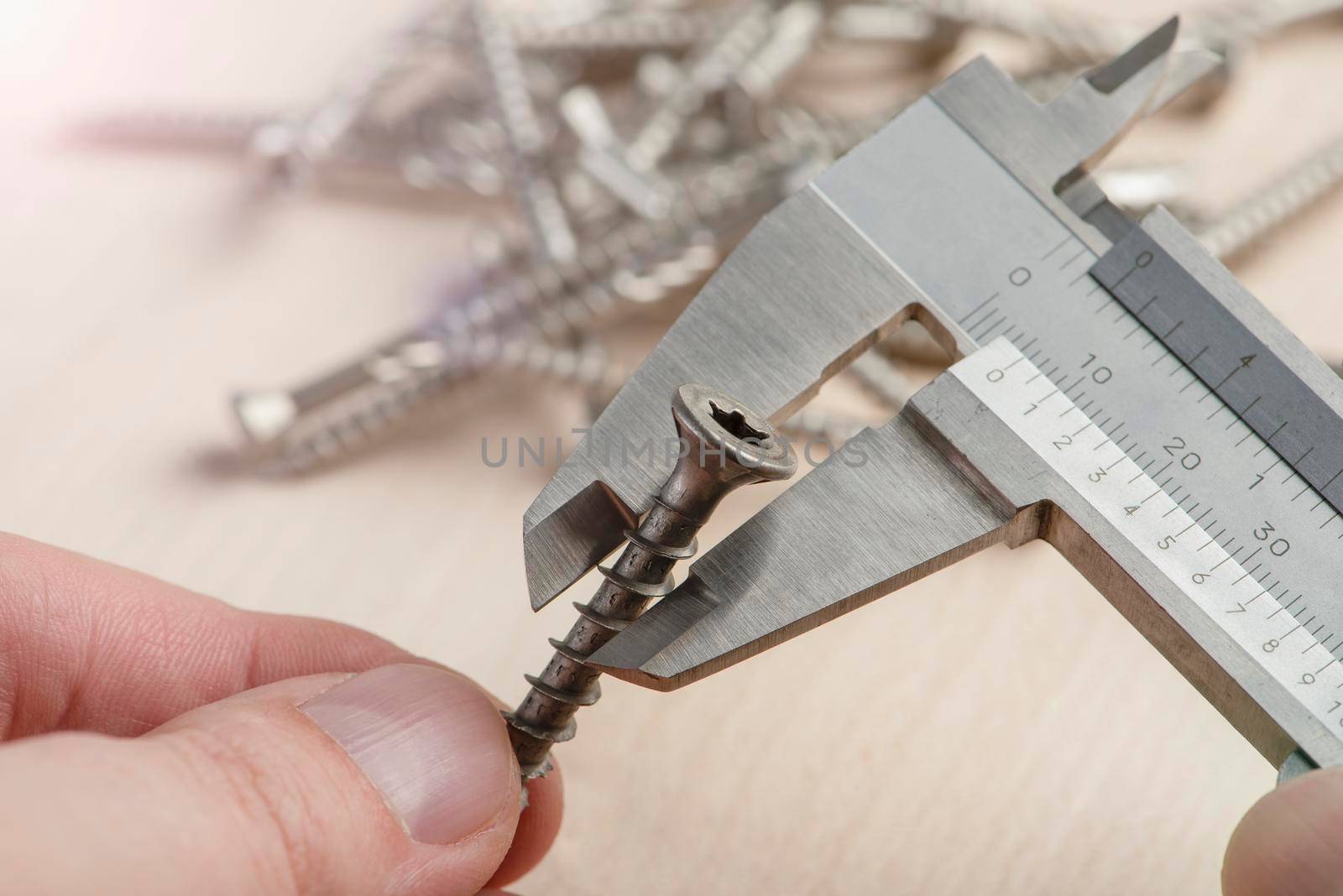 A man uses a caliper to measure the thickness of a screw with torx head. An accurate measuring device in the hands of a person against the background of screws scattered on the table.