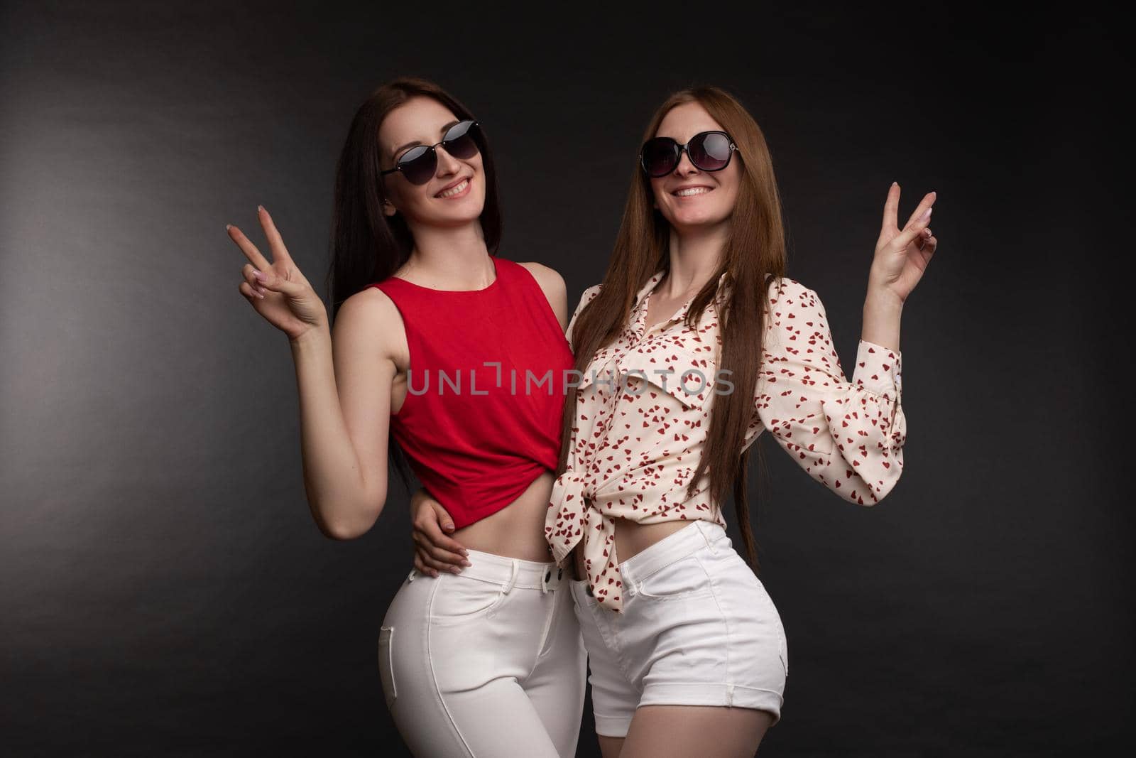 Two happy sisters in sunglasses holding hands and jumping. by StudioLucky