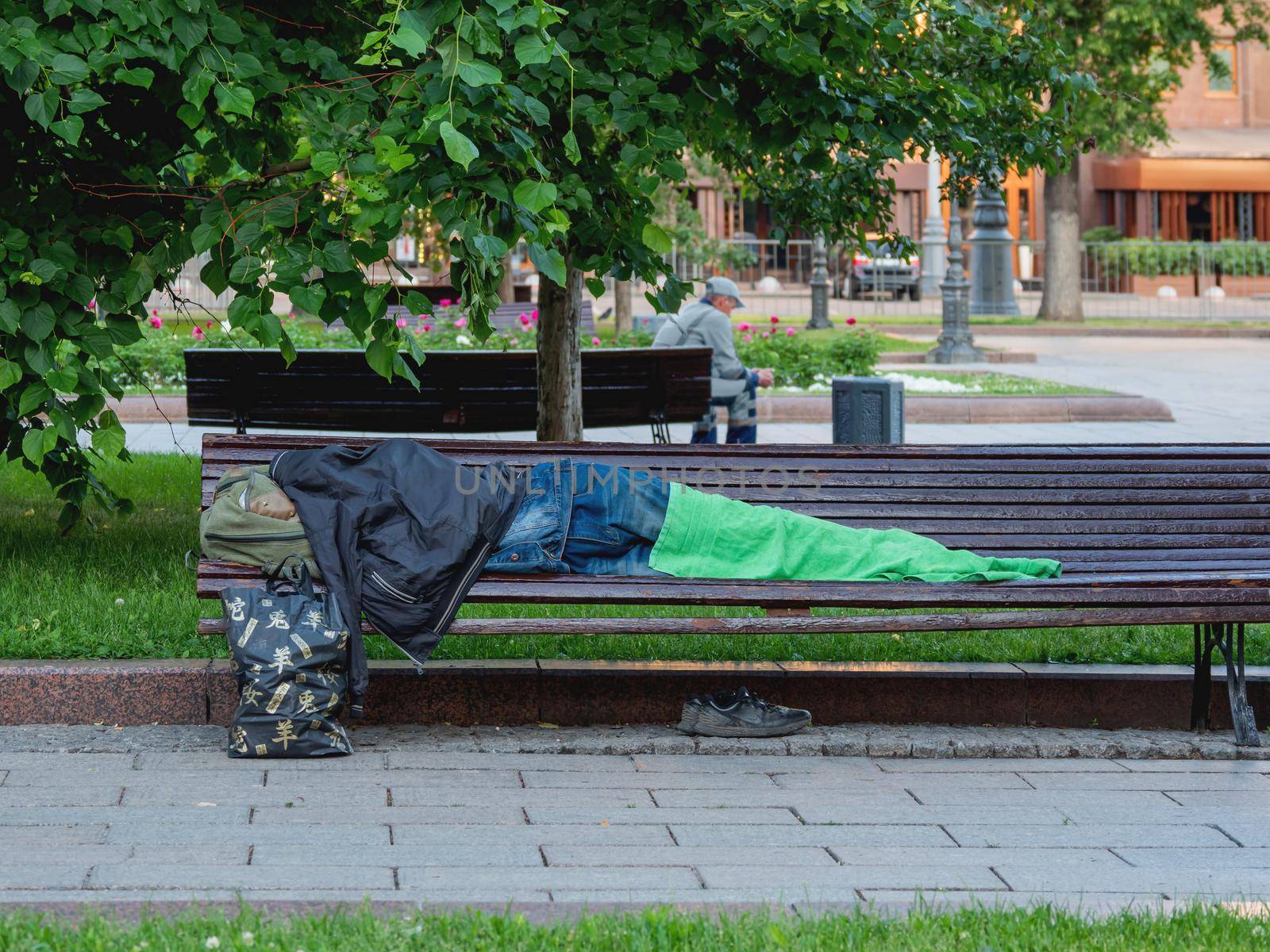 MOSCOW, RUSSIA - June 04, 2018. Homeless man sleeps on street bench. Houseless man covers himself with his clothes and towel. by aksenovko