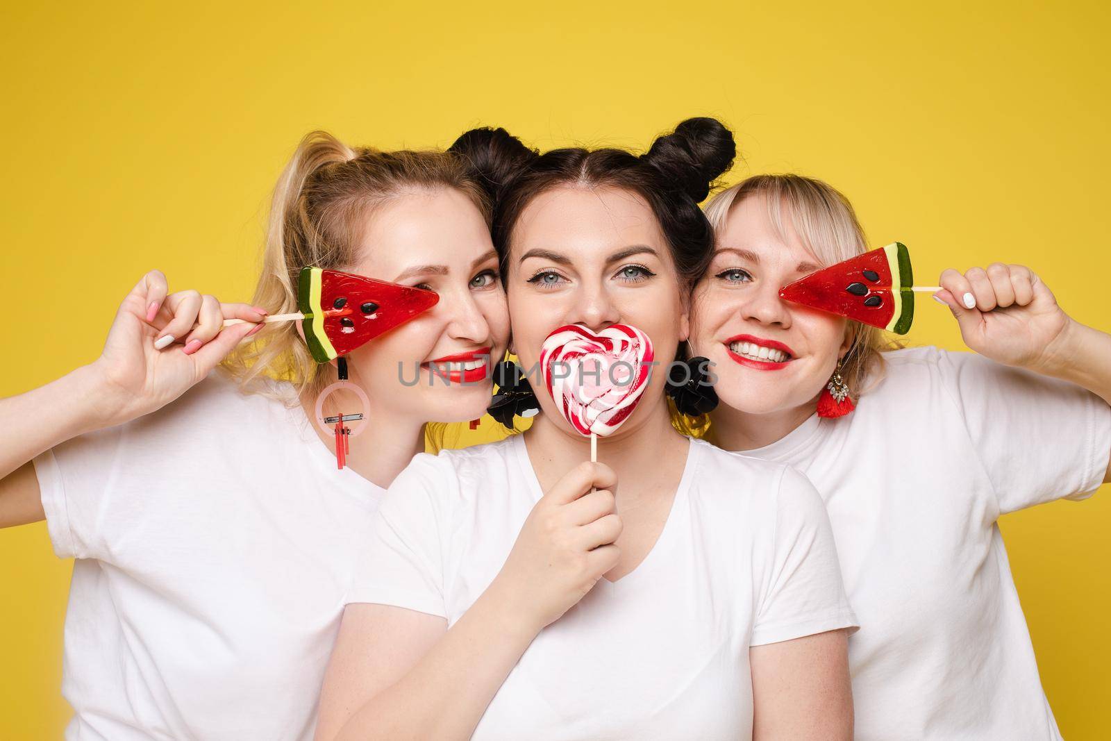 Three female friends celebrating a party event having fun and smiling with lolipops