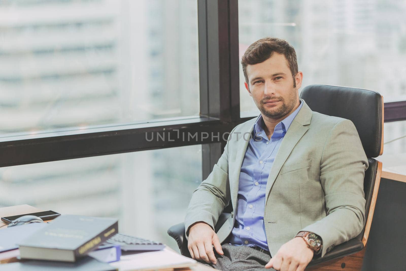 Businessman caucasion portait smile sitting in office looking camera city windows background