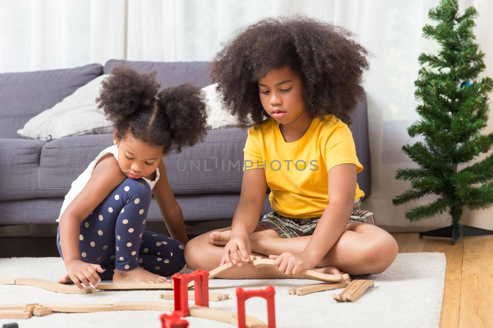 two black girl daughter kids playing train model together at living room.