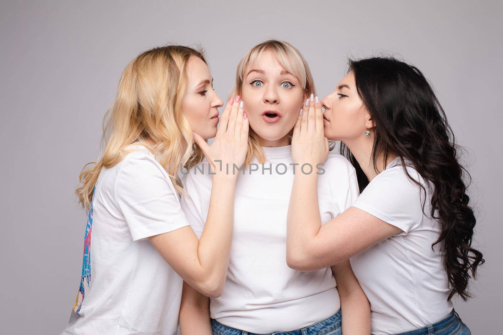Blonde girl in white shirt looking surprised while her friends are telling her a secret in studio.