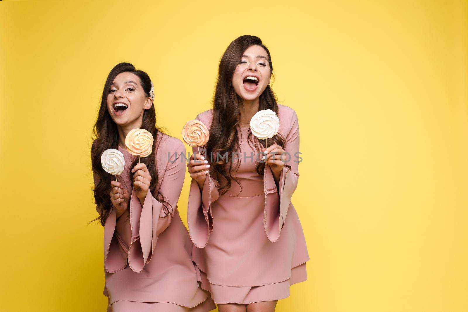 Charming twins closing eyes with lollipops and posing by StudioLucky