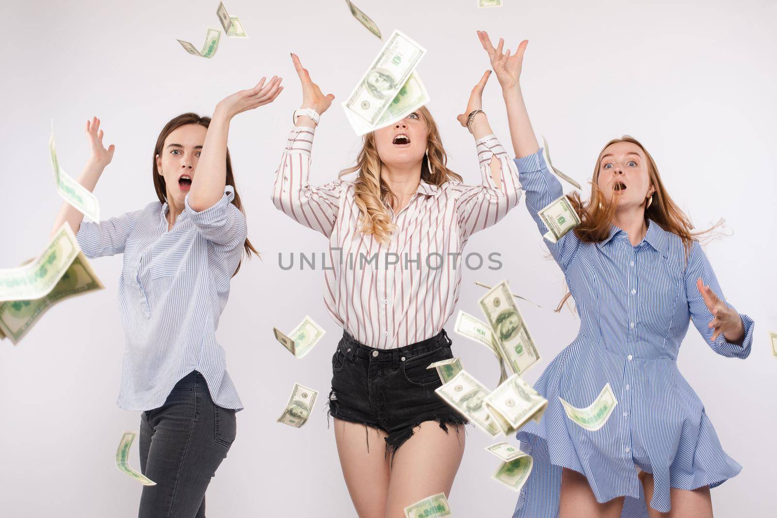 Three excited and shocked women with arms up trying to catch flying dollars or bucks in the air. Money flying in the air.