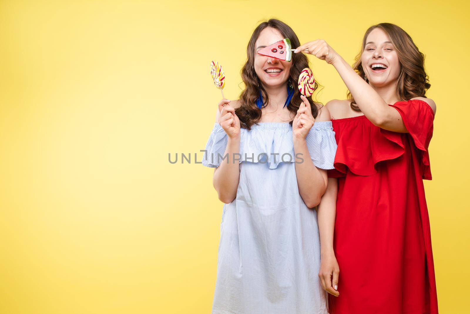 Horizontal portrait of two cheerful young women having fun together on background.