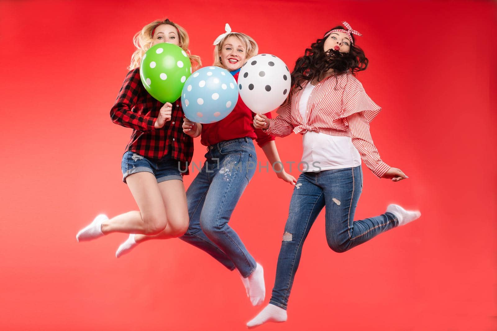 Laughing woman friend having fun jumping and smiling with colorful air balloon isolated at red studio background. Happy female teenager celebrating enjoying party posing together full shot