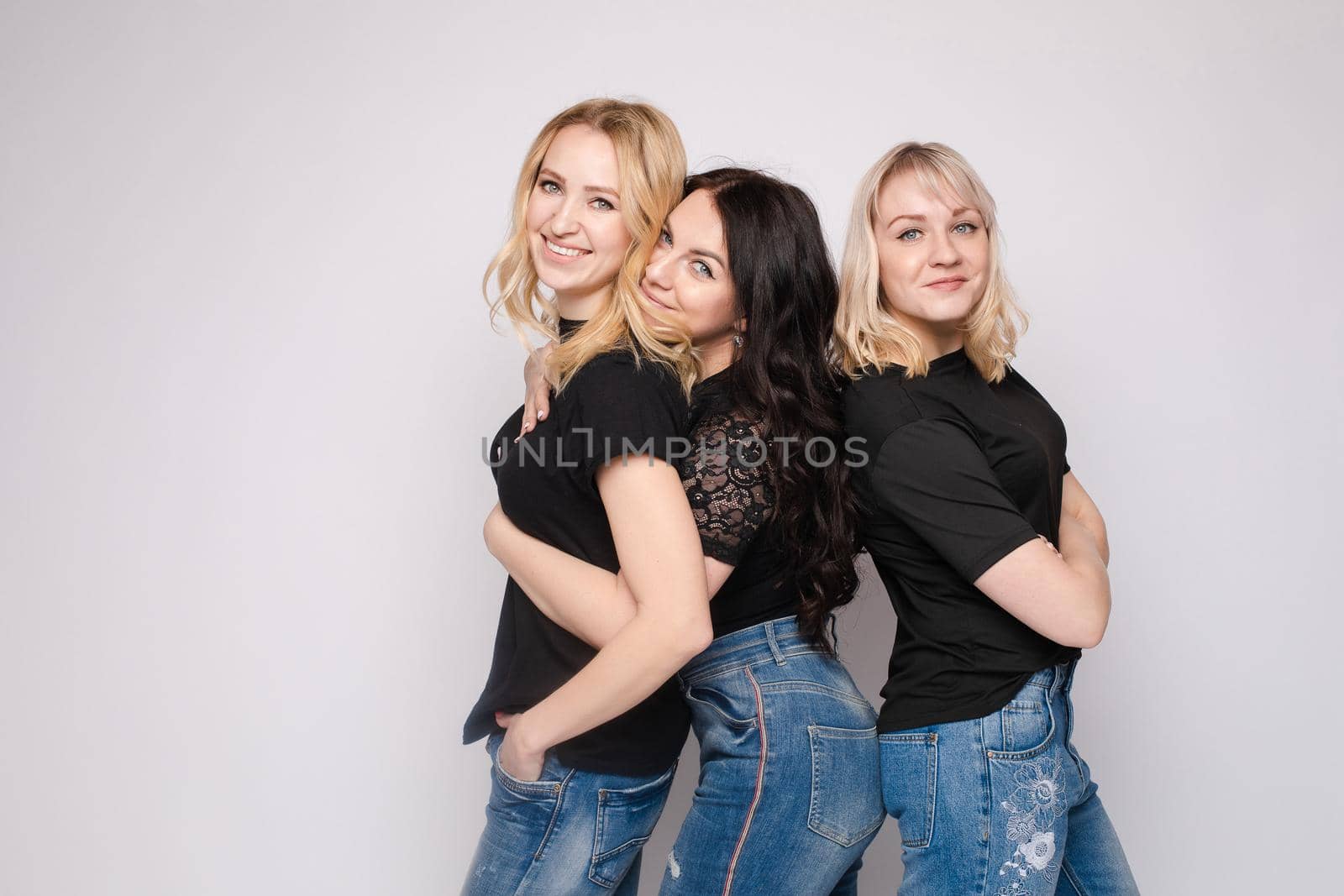 Group of smiling young friend woman hugging posing looking at camera at white studio background by StudioLucky