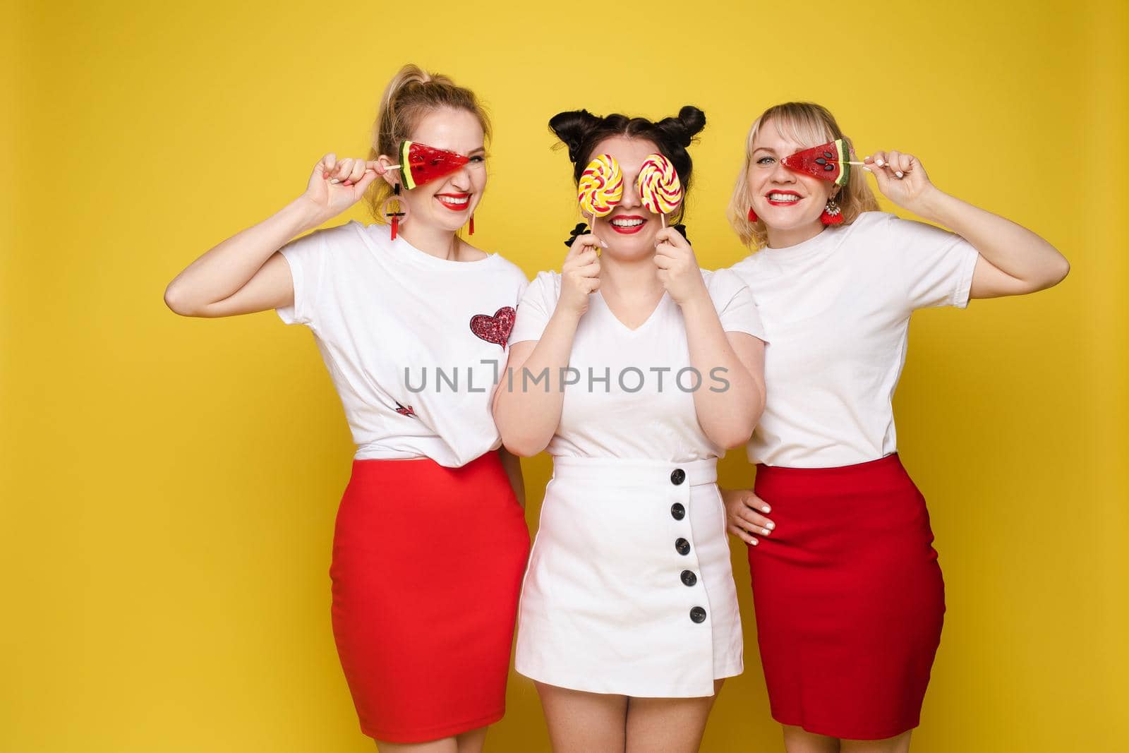 Group beautiful girl friend relaxing together posing with sweet colorful candy at yellow studio by StudioLucky