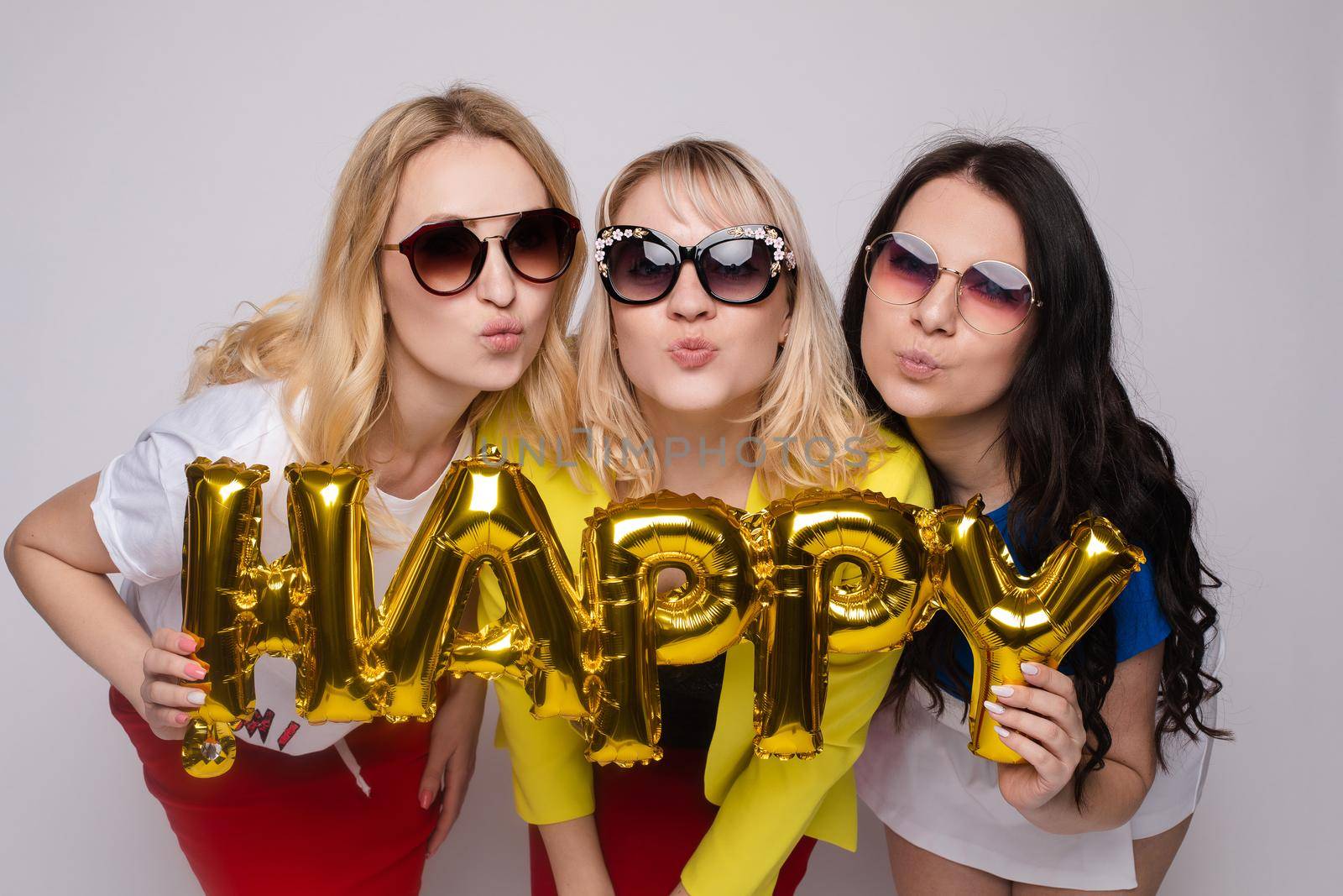 Group of stylish young woman wearing trendy sunglasses posing with big letters at white studio background medium shot. Happy adorable fashion girl having fun relaxing together enjoying friendship