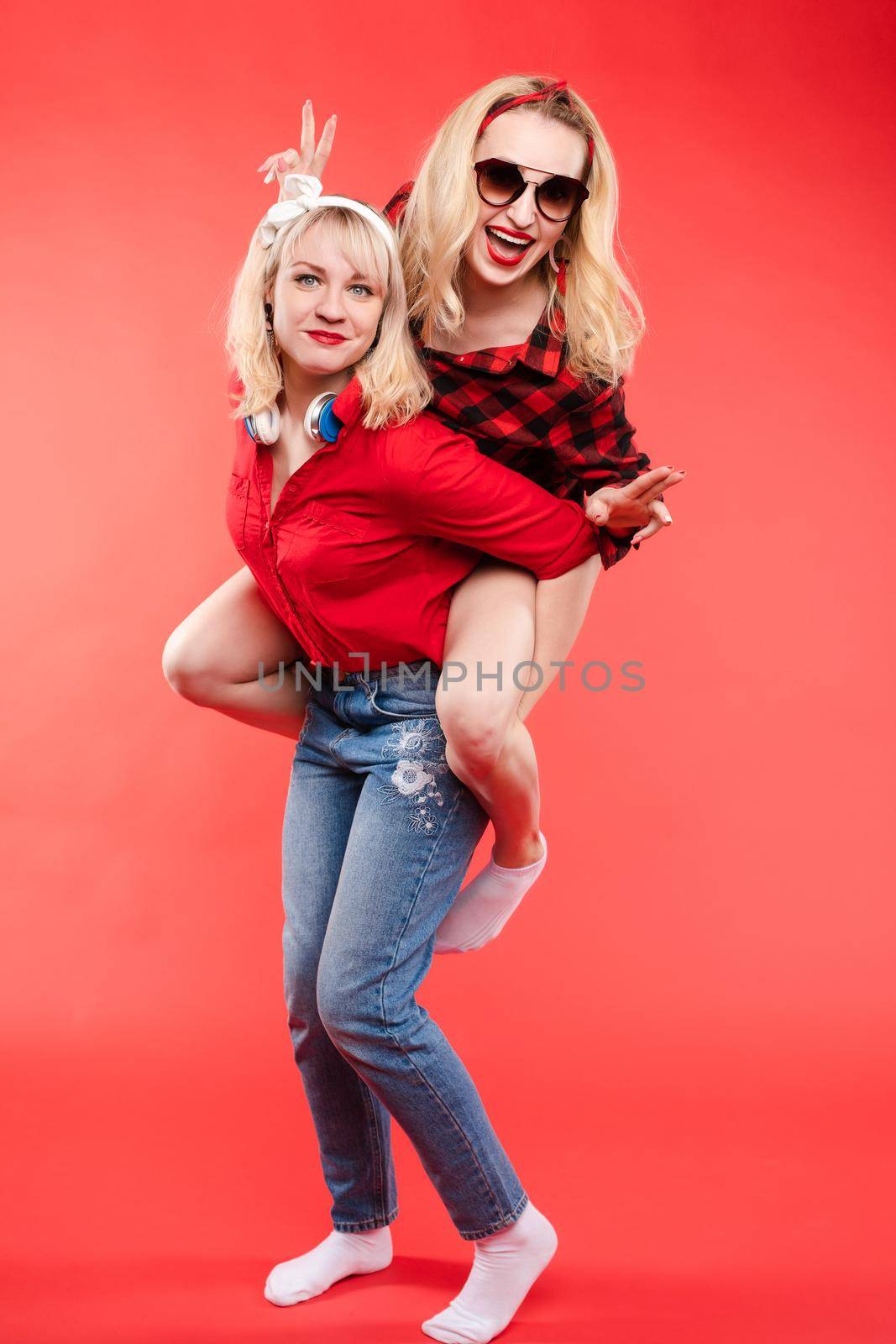 Friendly and trendy girls hugging over red background. by StudioLucky