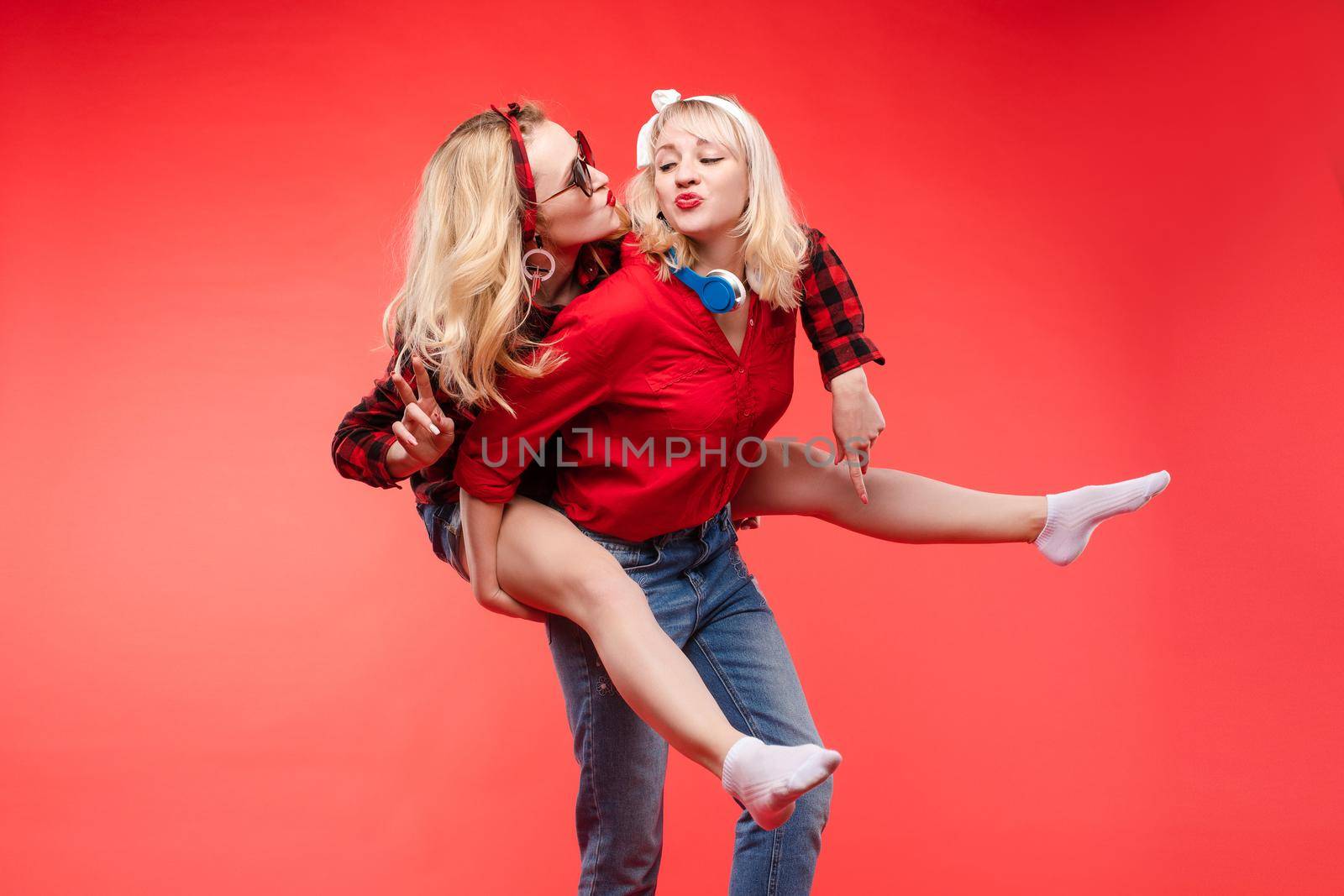 Sisters having fun giving piggyback.Stock studio portrait of two cheerful and positive trendy girlfriends or sisters having fun. by StudioLucky