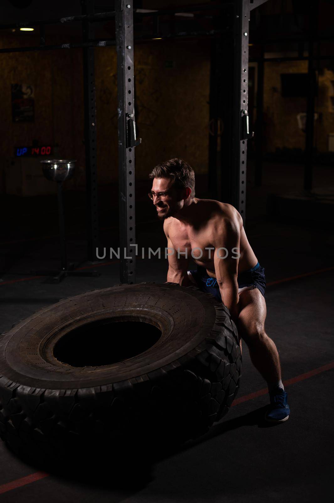 Caucasian man pushing a car tire in the gym. by mrwed54