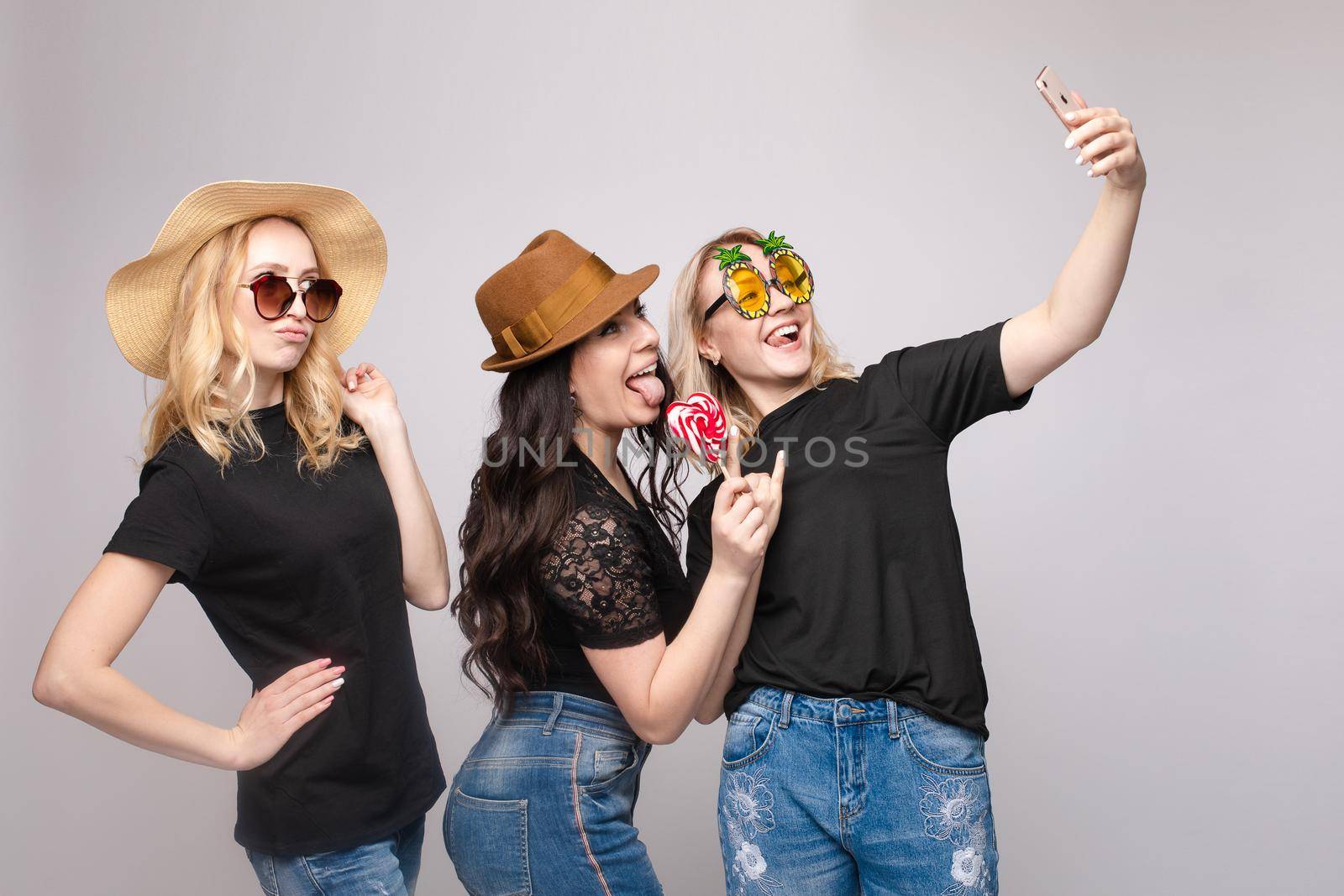 Smiling female friend wearing funny mask hat and eyeglasses posing taking selfie using smartphone medium shot. Happy woman having fun enjoying holiday party isolated at white studio background