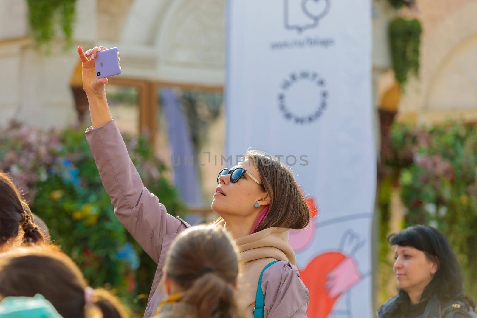 At a city festival, a girl photographs the stage with her mobile phone above her head from a height.Russia Zelenograd April 23, 2022.