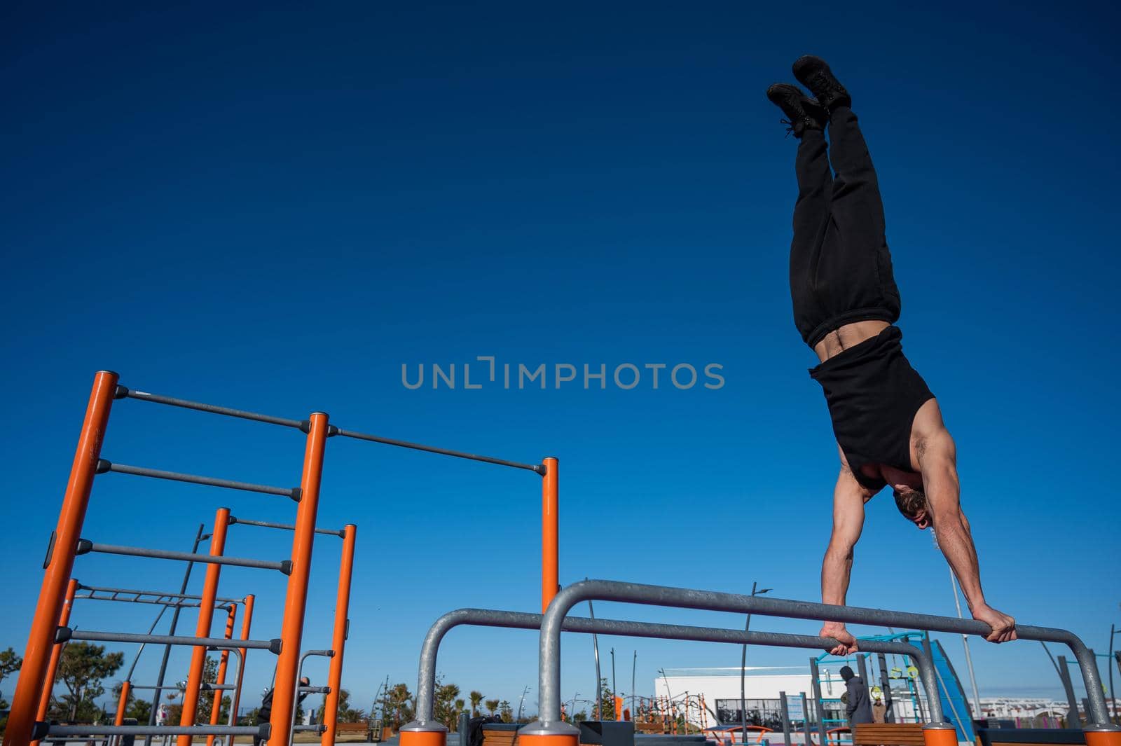 Shirtless man doing handstand on parallel bars at sports ground