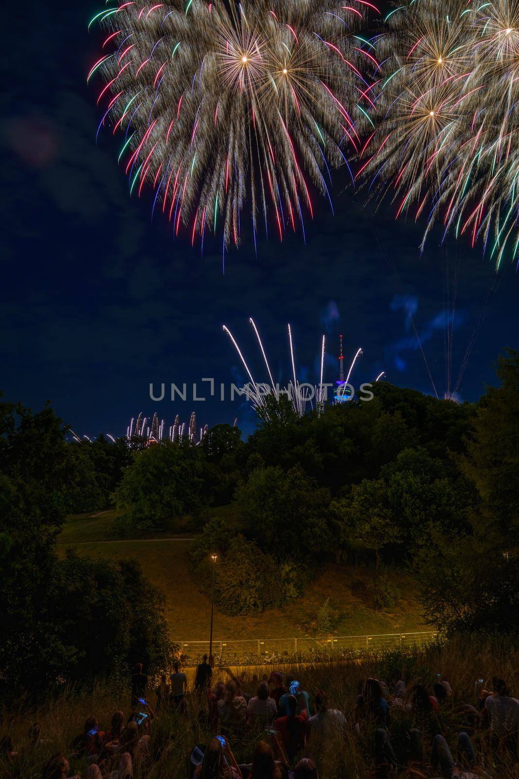 Colorful fireworks with people looking and the Munich Olympic Tower in the background, Munich, Germany by AllesSuper
