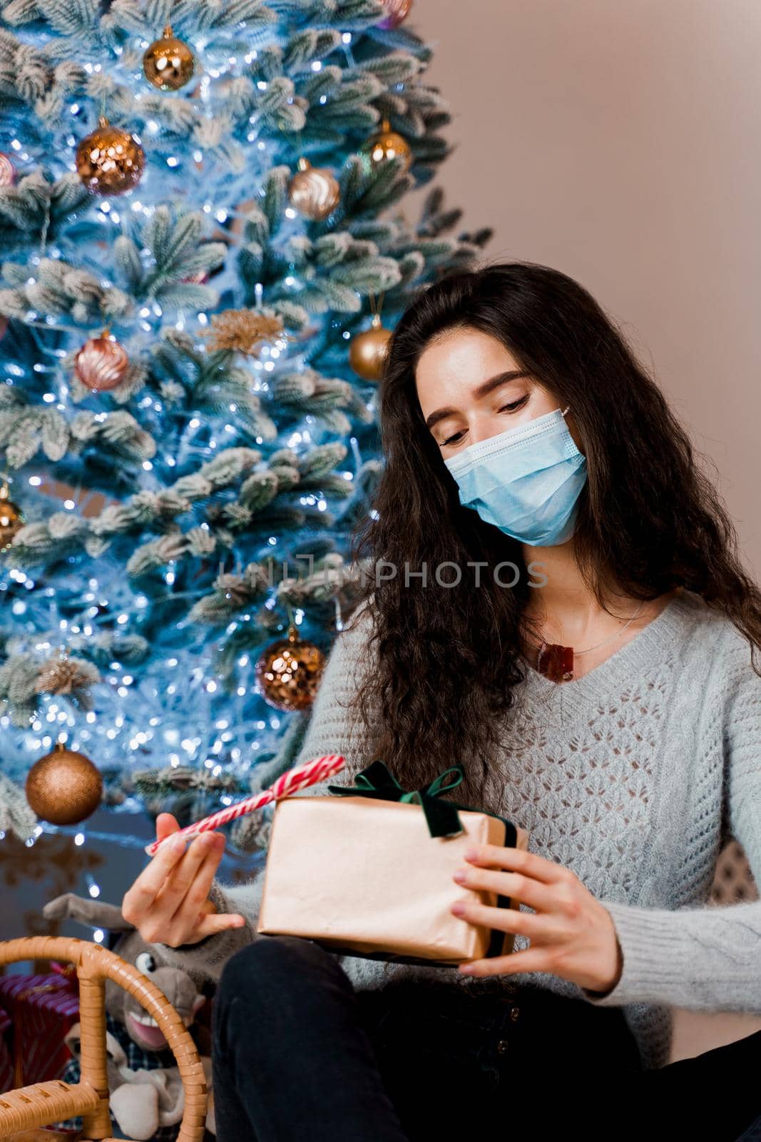 Girl in a medical mask with a Christmas present and candy. celebration of the new year on self-isolation. Pandemic coronavirus covid-19 concept. Advertising sale during the quarantine period