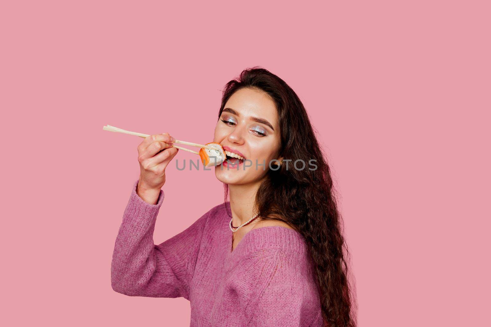 Girl is holding sushi by chopsticks and wanting to eat one piece of roll philadelphia. Sushi delivery. Eating japanese sushi set