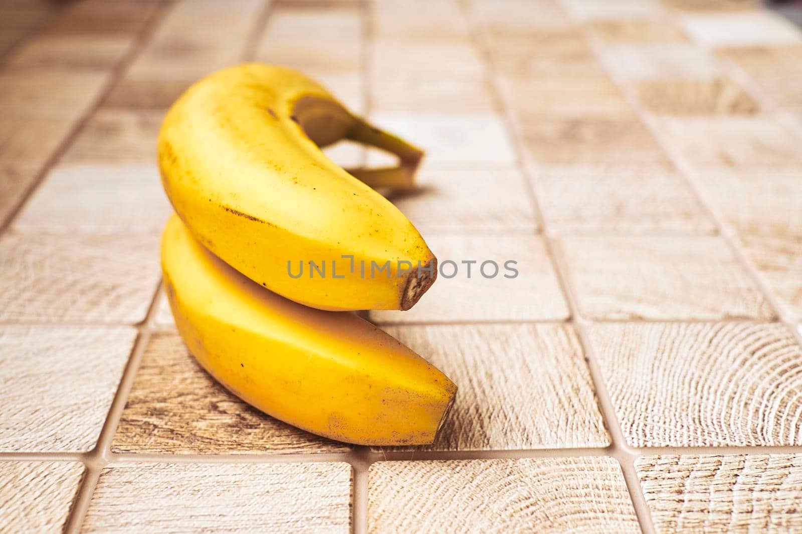 a long curved fruit which grows in clusters and has soft pulpy flesh and yellow skin when ripe.Two ripe bananas on a checkered wooden surface.