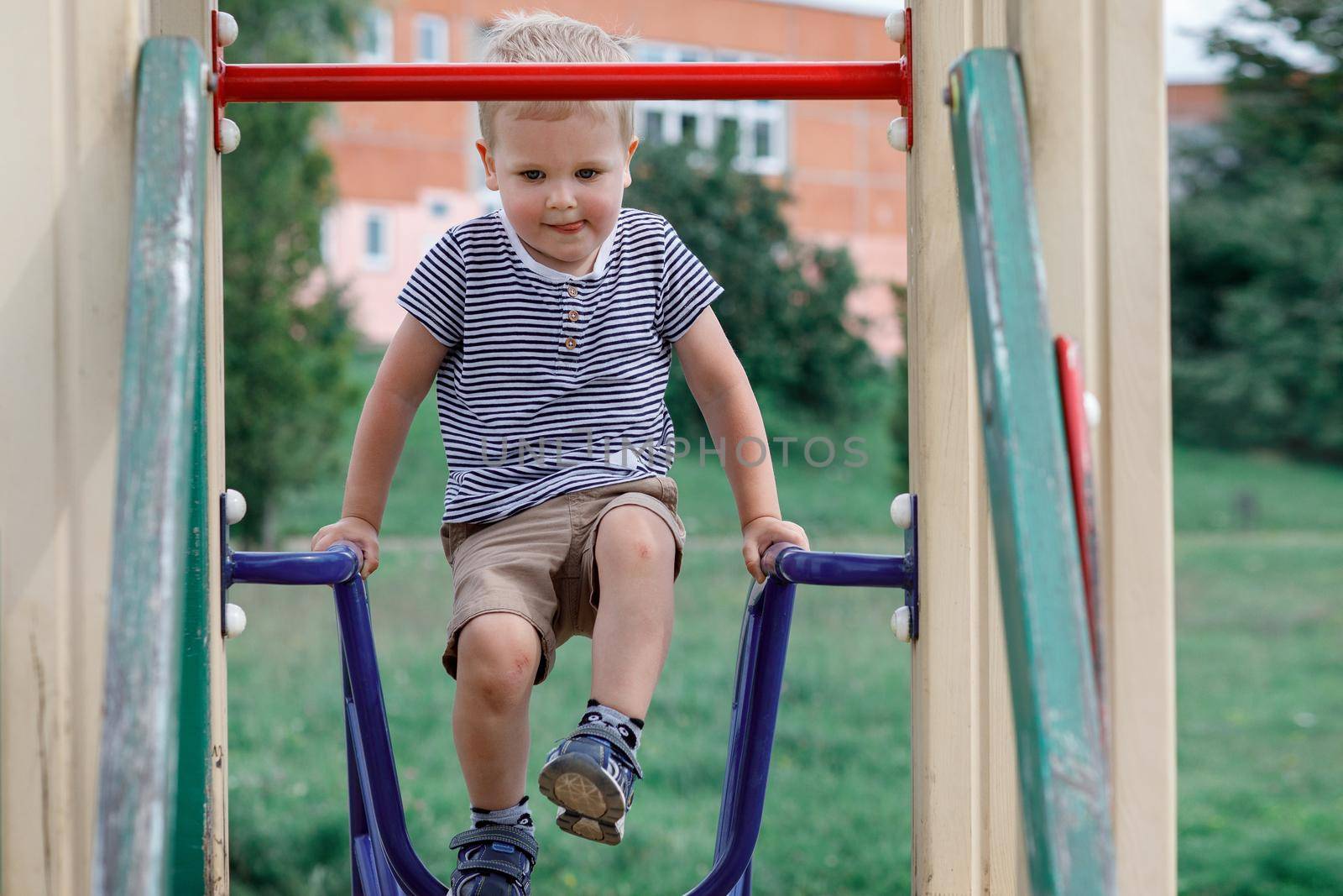 A small boy climbs up to playhouse at public playground in summer time