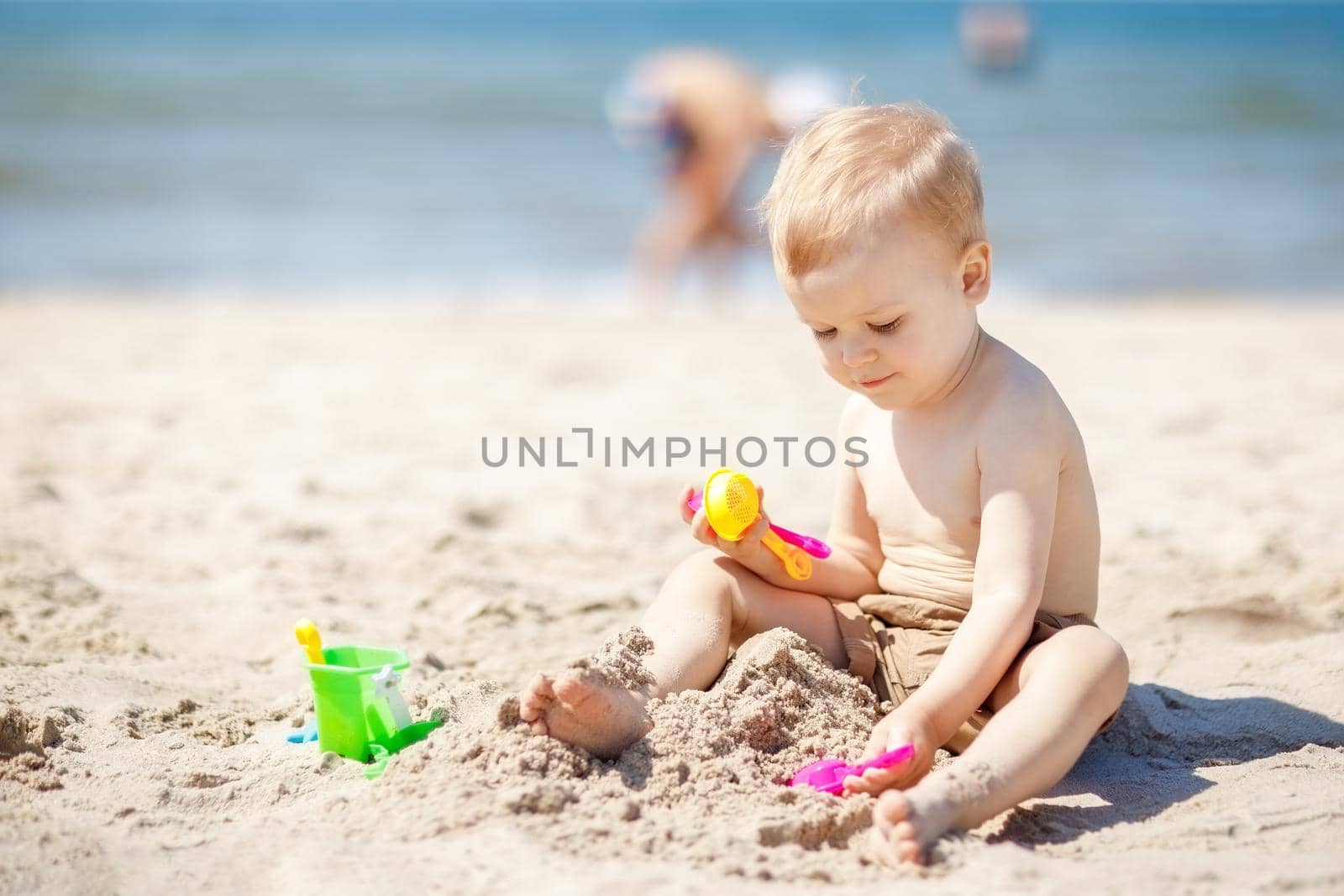 Kid playing on beach with sand. Sand and water toys. No sun protection for young child. Little boy digging sand, building castle at sea shore.