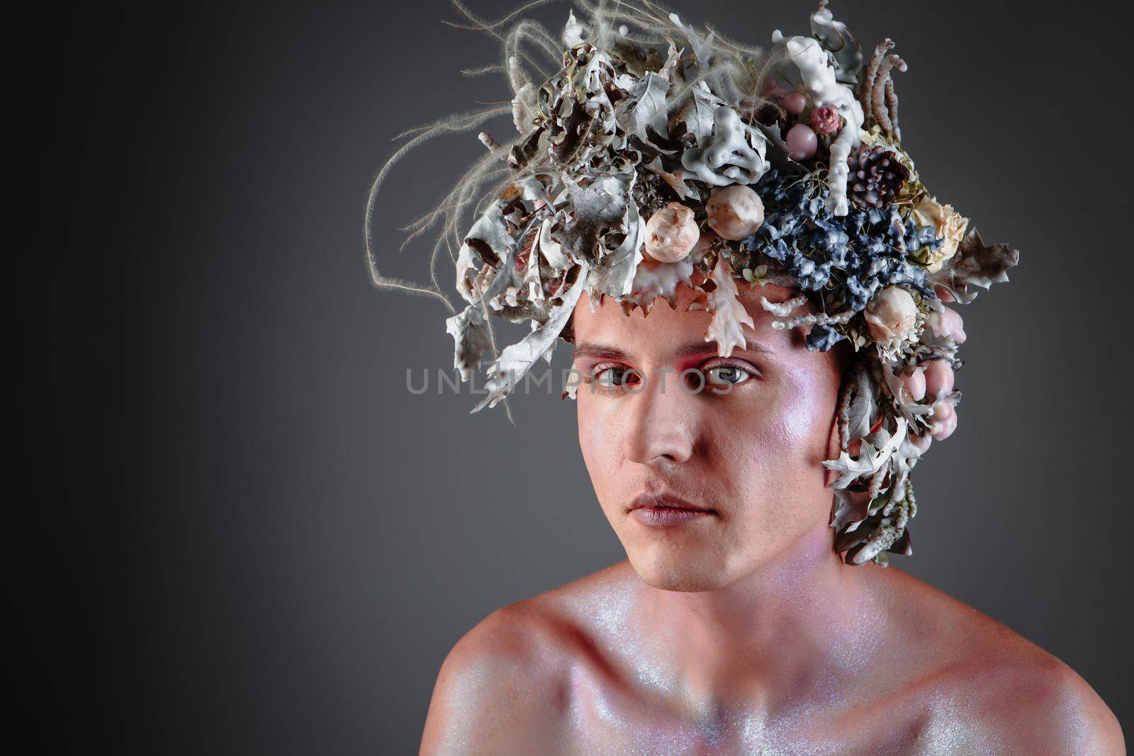 The face of a male model in a headdress of fresh flowers filled with wax