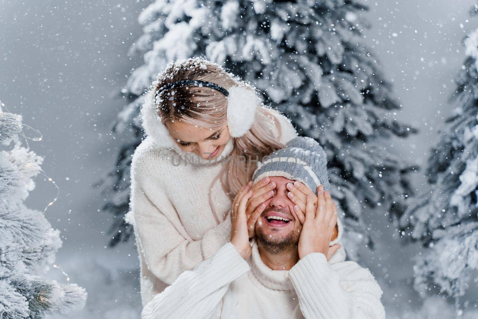 Couple seat on the snow and hug, kiss, and have fun each other. Winter love story before new year celebration. Waiting for christmas gift. Happy couple weared fur headphones, hats, white sweaters.