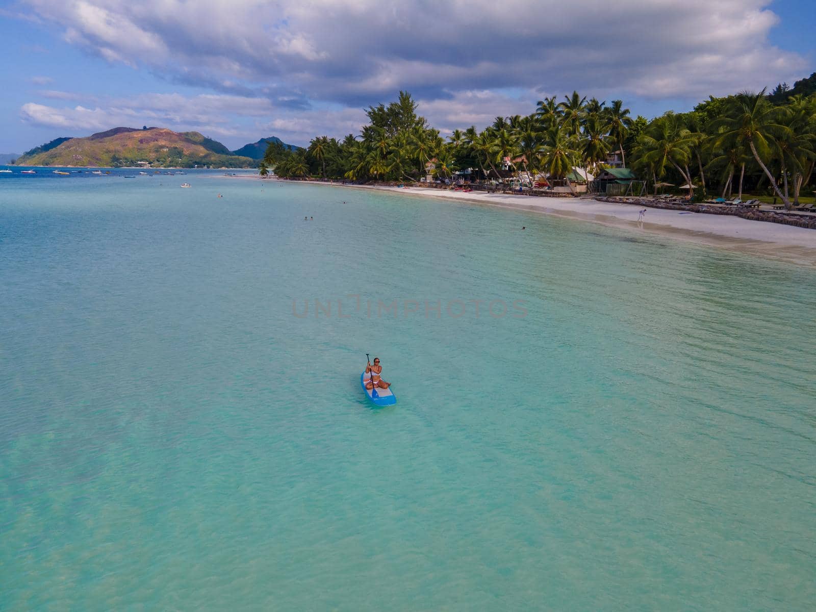 woman with paddleboard sup in ocean, Praslin Seychelles tropical island with withe beaches and palm trees, the beach of Anse Volbert Seychelles.