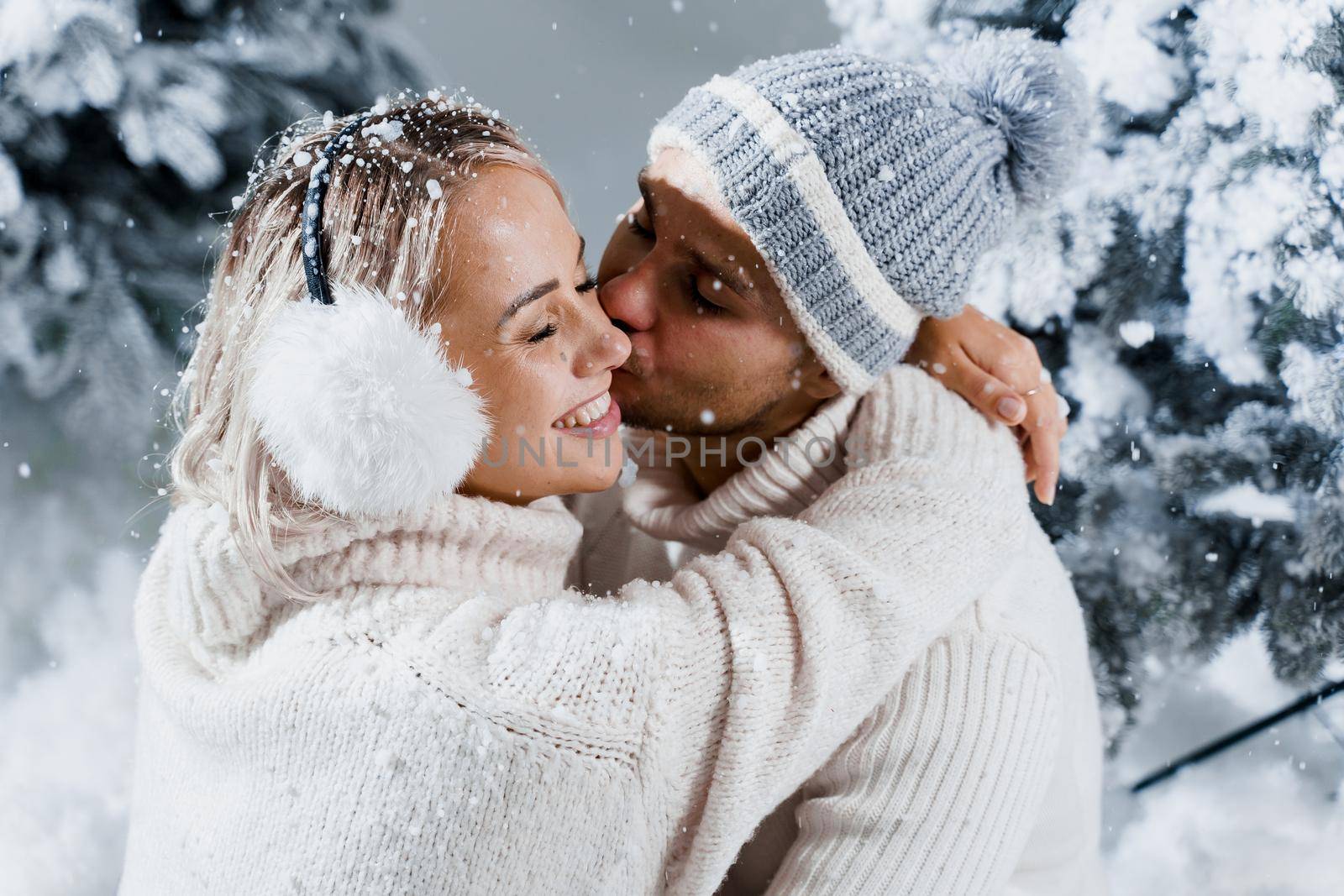 Winter love story at the eve of new year celebration. Couple hugging near christmass trees. Winter holidays. Love story of young couple weared white pullovers. Happy man and woman love each other.