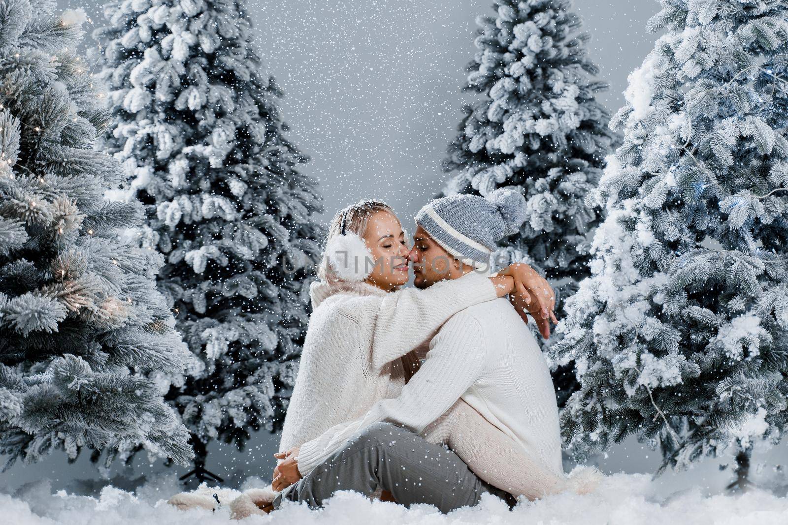 Couple hugging near christmass trees. Winter holidays. Love story of young couple weared white pullovers. Happy man and young woman love each other.
