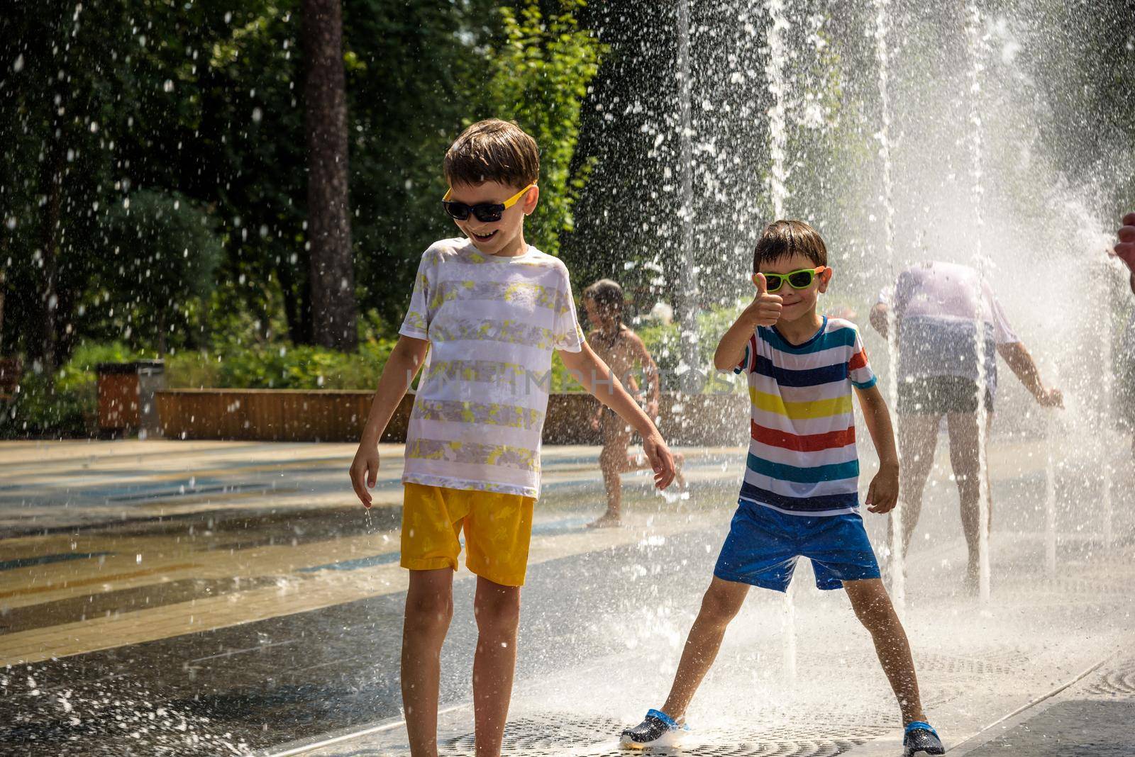 Kyiv, Ukraine - August 01, 2021: Boys jumping in water fountains. Children playing with a city fountain on hot summer day. Happy friends having fun in fountain. Summer weather. Friendship, lifestyle and vacation.